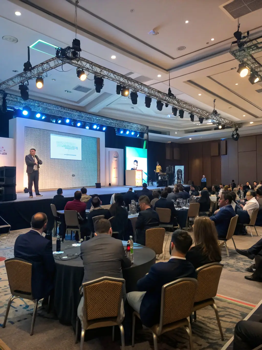A photograph of a modern conference venue with a stage set for a keynote speaker, displaying a banner with the conference name 'Global Investment Summit 2026'.